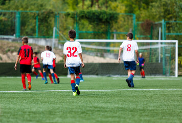 Young sport boys in white and red sportswear running and kicking a  ball on pitch. Soccer youth team plays football in summer. Activities for kids, training	