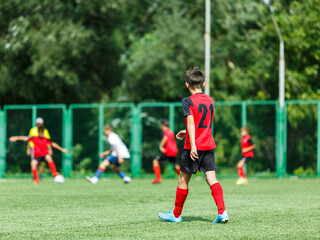 Obraz premium Young sport boys in white and red sportswear running and kicking a ball on pitch. Soccer youth team plays football in summer. Activities for kids, training 