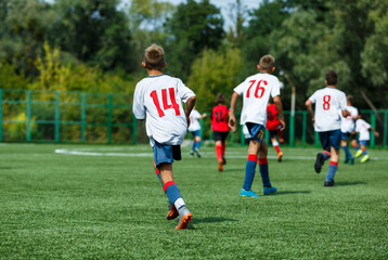 Young sport boys in white sportswear running and kicking a  ball on pitch. Soccer youth team plays football in summer. Activities for kids, training	