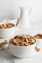 Bowls with tasty cornflakes, almond and milk on light background