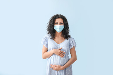 Pregnant woman wearing medical mask on color background