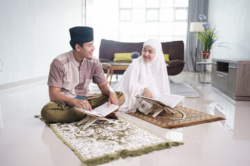 Asian Muslim man teaching woman reading Koran or Quran in living room. muslim couple praying at home