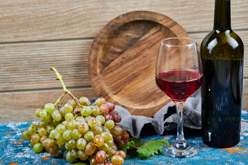 Bunch of grapes, a glass of red wine and a bottle of wine on blue 