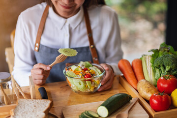 Closeup image of a beautiful young asian female chef cooking and eating fresh mixed vegetables salad in kitchen