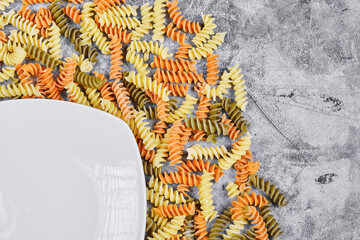 Colorful fusilli and white plate on marble background