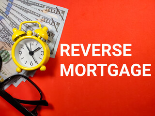 Selective focus.Word REVERSE MORTGAGE with clock,glasses and dollar banknote on red...