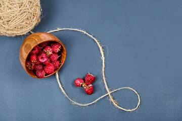 Sweet raspberries in the wooden bowl on the grey background with wool