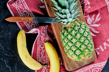Ripe pineapple and bananas on wooden board with red tablecloth
