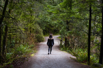 Obraz premium Girl Walking on a Beautiful Path in the Rainforest during a wet and rainy day. Lynn Canyon Park, North Vancouver, British Columbia, Canada. Nature Forest Background