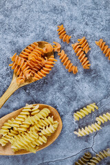 Raw fusilli and wooden spoon on blue background
