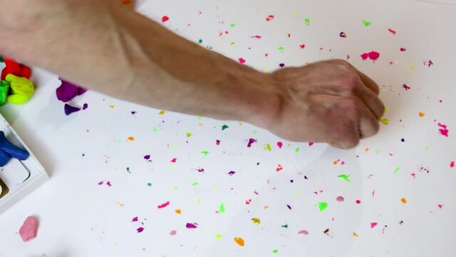 dots from multi-colored plasticine, put by a man's hand on a white table