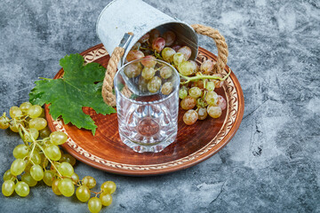 Small bucket of grapes inside ceramic plate and a glass on a marble background