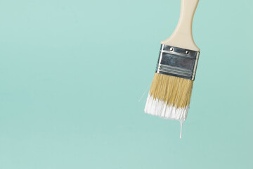 Brush with dripping white paint on a blue background.