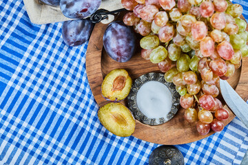 Fresh plums and a bunch of grapes on a wooden plate