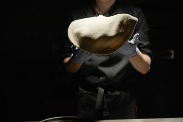The chef tosses the pizza dough into the air. A man in the kitchen in a restaurant prepares pizza.