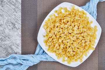 A plate of uncooked pasta with blue tablecloth on marble table