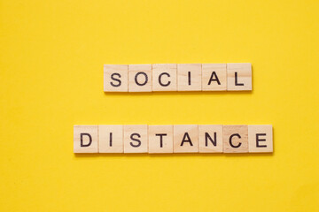 Word SOCIAL DISTANCE made from wooden letters on yellow background.