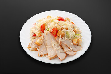 Caesar salad on a white plate. Chicken fillet, cherry tomatoes, salad mix, croutons, parmesan cheese, sauce. Dark background. Isolated. Close-up.