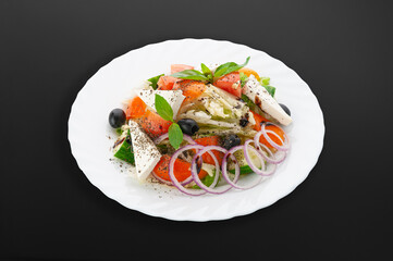 Greek salad on a white plate..Tomatoes, cucumbers, bell peppers, salad mix, feta cheese, olive oil. Dark background. Isolated. Close-up.