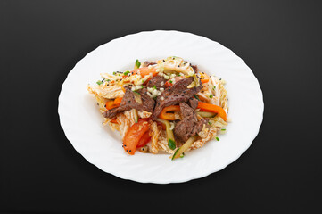 Veal salad on a white plate..veal fillet, tomatoes, fresh cucumbers, salad mix, green onions, sesame seeds, sauce. Dark background. Isolated. Close-up.