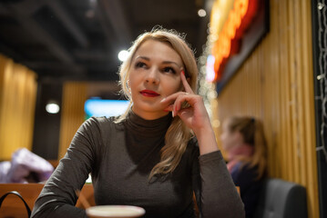 Young beautiful blonde girl drinks coffee in the evening in a cafe.