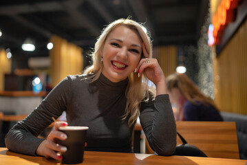 Young beautiful blonde girl drinks coffee in the evening in a cafe.