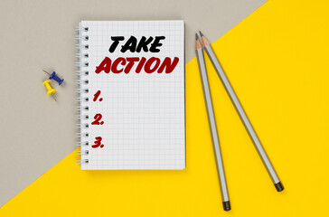 On a yellow-gray background are pencils, buttons and a notebook in which it is written - TAKE ACTION
