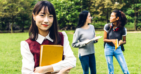 Smiling woman international students or teenagers standing and holding book smiling at camera with group of students in park at university.Education and friendship Concept