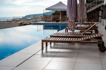 Luxury infinity pool and wooden deck chairs at the resort with beautiful sea views. The concept of...