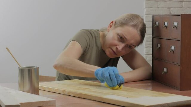 A woman carpenter, designer, decorator, works in a workshop, covers the wooden surface with oil.