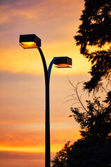Illuminated street light with double lamps and pole against sunset sky.