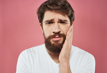 Obraz premium A man with a beard touches his face with his hand on a pink background