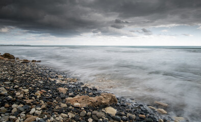 Obraz premium Seawaves splashing to the coast with stones against stormy dramatic cloudy sky. Wintertime, Limassol cyprus