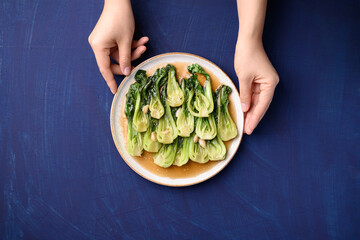 Stir fried bok choy with soy sauce on plate holding by hand on blue background, Asian vegan food, Top view