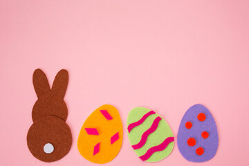 Easter. Cut out of felt applications of colourful eggs and brown rabbit. Pink background. Flat lay. Copy space