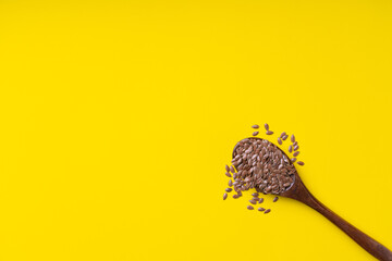 flax seeds in a dark wooden spoon on a yellow background