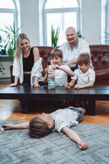 Warm portrait of joyful and happy family playing board game at table. Cheerful boy lying on floor with outstretched arms.