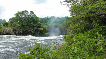 The Zambezi River flows rapidly before falling into the abyss. Foam and spray. Over the edge of the gorge there is a mist of water spray. Around - tropical vegetation. Victoria Falls. Zambia