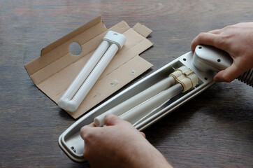 An adult male removes a burned-out compact fluorescent lamp from a table lamp.