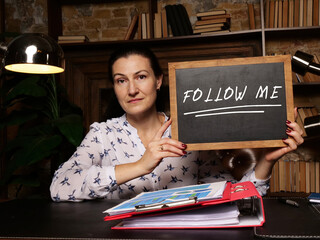 Woman showing black chalkboard with written text FOLLOW ME . Blurred background. Horizontal mockup