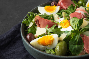 Prosciutto salad with parmesan cheese, olives, eggs and arugula in a plate on black background. Italian food snack