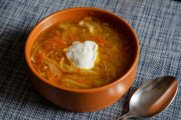 Cabbage soup with sour cream in a brown earthen bowl on a blue tablecloth.