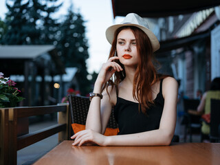 Romantic woman in a cafe on the street and bright makeup watches a white hat