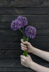 The palms of the hands hold a bouquet of lilac flowers on a wooden background.