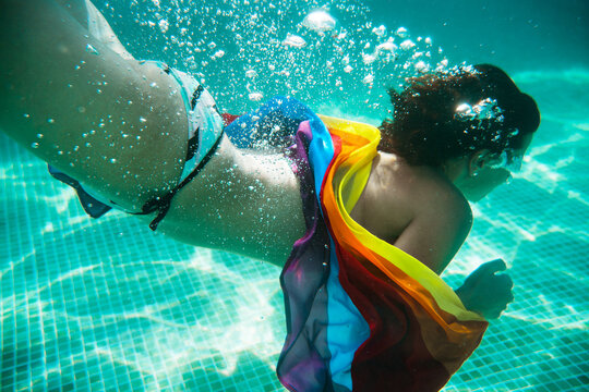 Horizontal view of unrecognizable woman diving into water holding a colorful lgbt flag. Lesbian, gay, bisexual and transgender iconic colors. Gay pride and summer holidays concept.