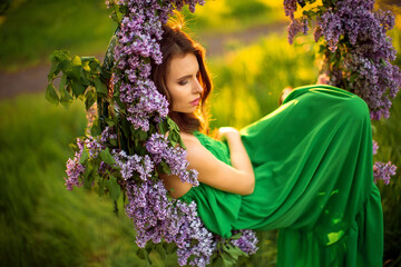 attractive woman in green dress posing near lilac flower decor.