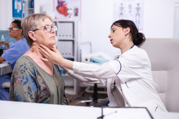 Fototapeta premium Young medic palpating neck of senior woman, elderly patient visiting doctor at hospital checking thyroid throat touching health at clinic. Healthcare specialist, medicare, treatment medical concept.