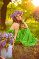 Fototapeta premium attractive woman in green dress posing near lilac flower decor.