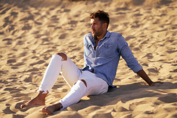 Attractive man sitting on the sand of the beach