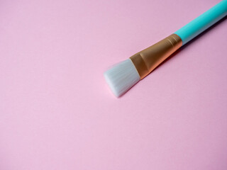 Obraz na płótnie Canvas A blue cosmetic brush for applying face masks lies on a pink background. Cosmetic accessories, space for text, copy space